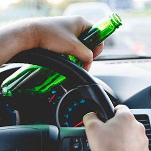 Hands on a steering wheel holding a beer bottle, symbolizing a first-time DWI
