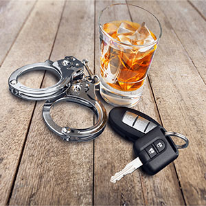 Handcuffs, car keys, and alcohol glass on wooden table; drunk driving legal charges